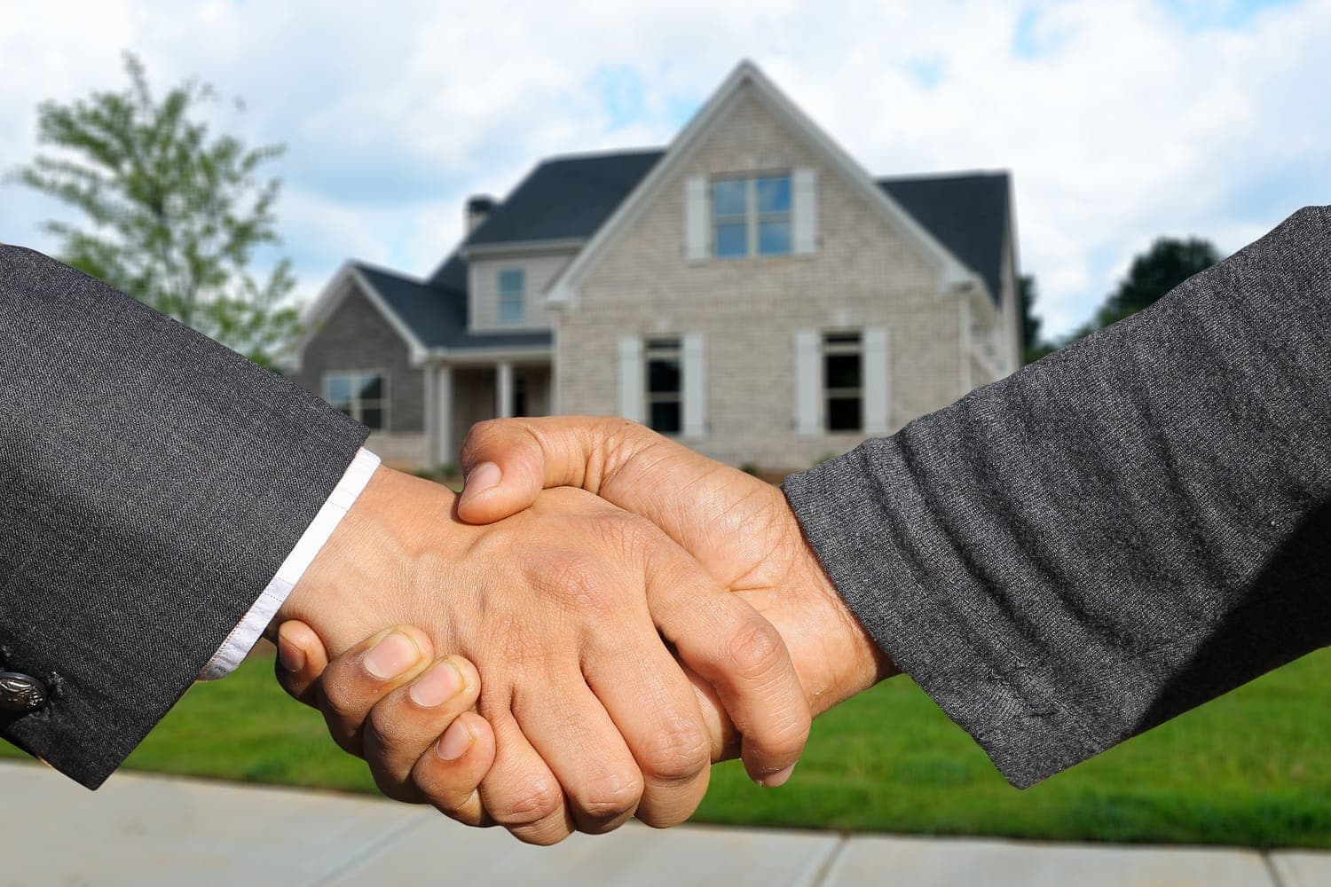 Buyer and agent shaking hands in front of a house